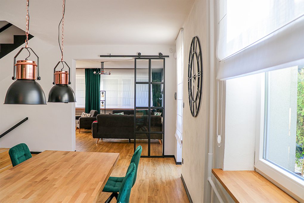 black metal wall clock, industrial style clock, loft decor, metal door with glass, loft door, metal glass sliding door, black frame glass door, green dining chairs, open living room to dining room, dining room industrial hanging lamps, large wooden dining table
