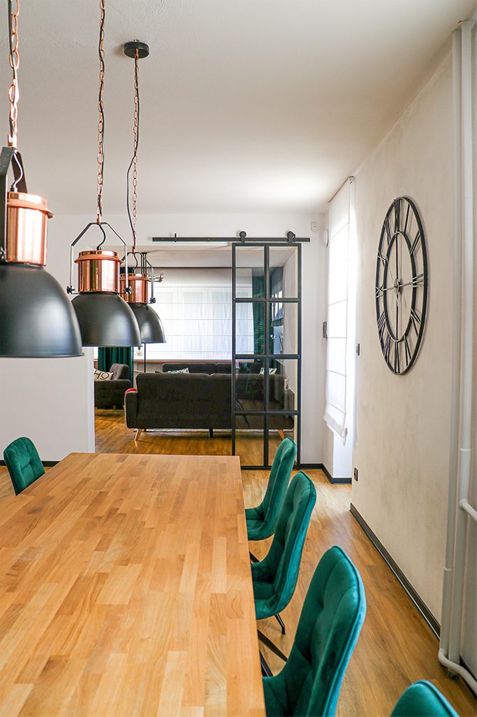 black metal wall clock, industrial style clock, loft decor, metal door with glass, loft door, metal glass sliding door, black frame glass door, green dining chairs, open living room to dining room, dining room industrial hanging lamps, large wooden dining table