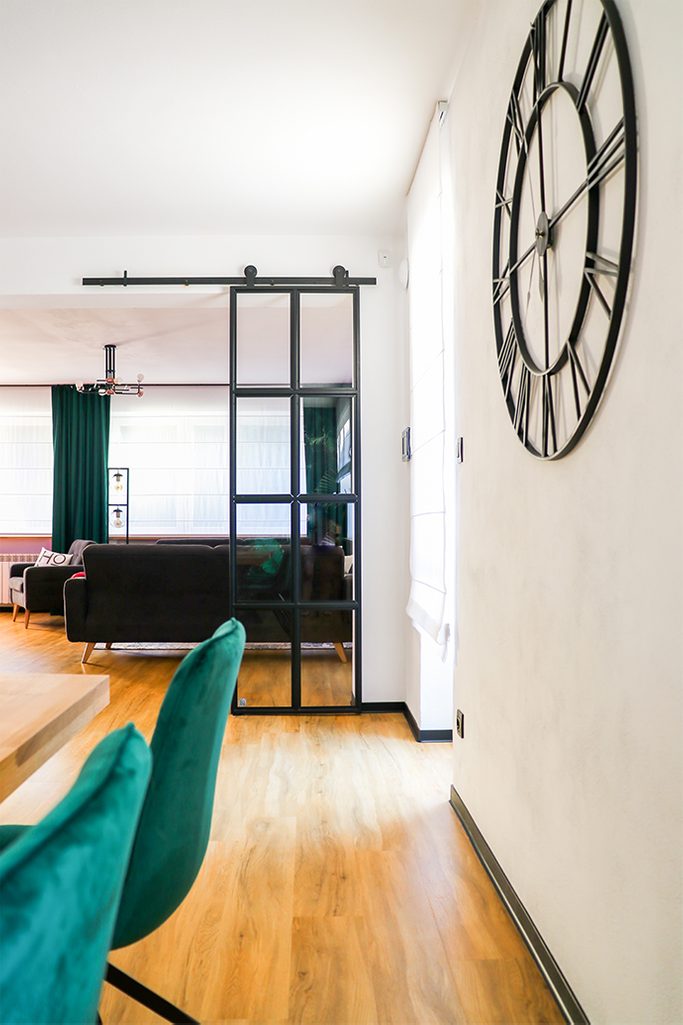 black metal wall clock, industrial style clock, loft decor, metal door with glass, loft door, metal glass sliding door, black frame glass door, green dining chairs, living room open to dining room, green curtains