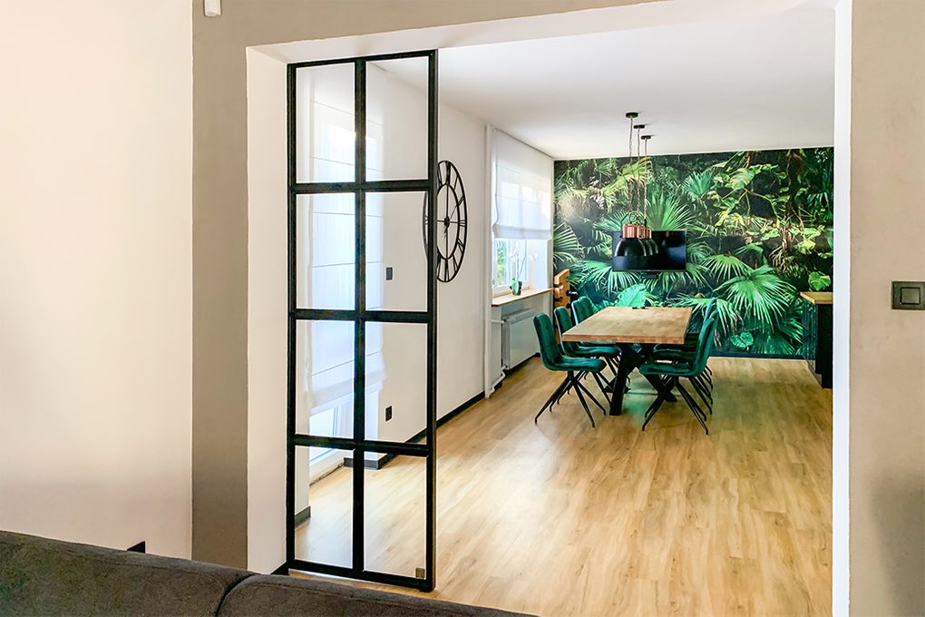 living room open to dining room, open living room, glass and metal sliding doors, metal sliding doors with glass, loft doors, industrial hanging lamps for dining room, botanical wallpaper, decorative wallpaper, large wooden table, green dining chairs