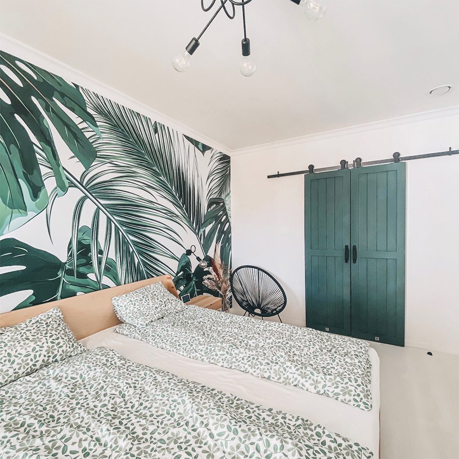 green doors, bedroom with wardrobe, sliding door to the walk-in wardrobe, sliding door in the bedroom, greenery in the bedroom, industrial chandelier in the bedroom, decorative wallpaper with plants, botanical wallpaper, green wallpaper for the bedroom, openwork chair, plant motif on bedding, green color bedroom