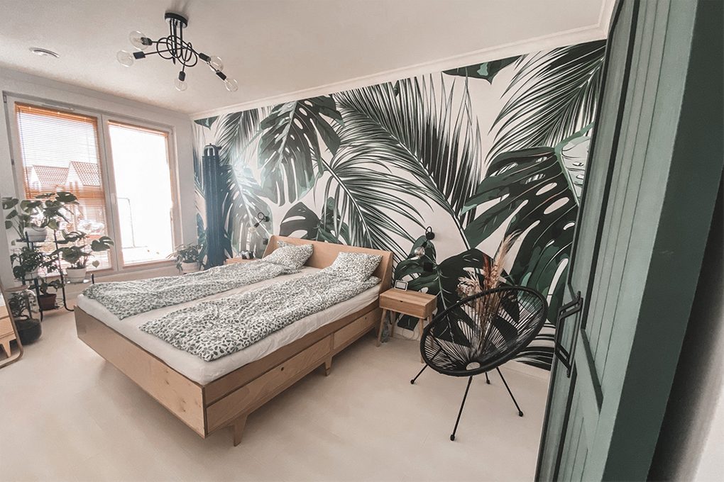 green doors, light wood in the bedroom, light wood and greenery, greenery in the bedroom, plant motif in the bedroom, botanical wallpaper, decorative wallpaper in the bedroom, linen with a floral motif, plant in the bedroom, industrial chandelier in the bedroom, black openwork chair, light wooden bed, small bedside table made of light wood