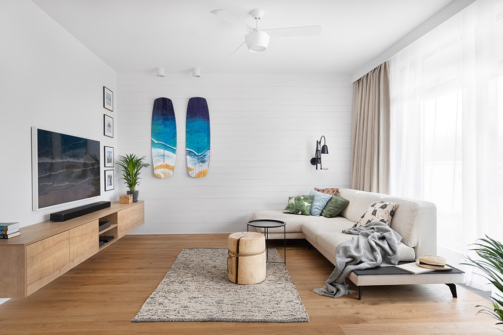 large and bright living room, white walls in living room, blue decorative surfboard on the wall, wooden coffee table, large sofa