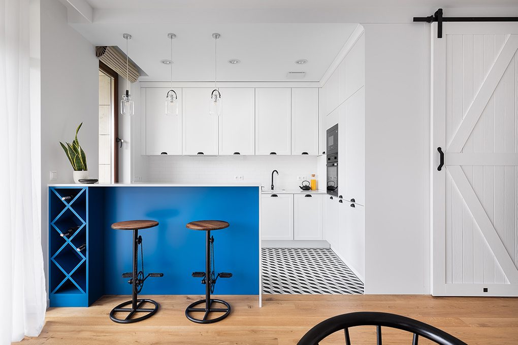 white kitchen with black accessories, white sliding door to utility room, blue accents in kitchen, industrial bar stool with bike pedals