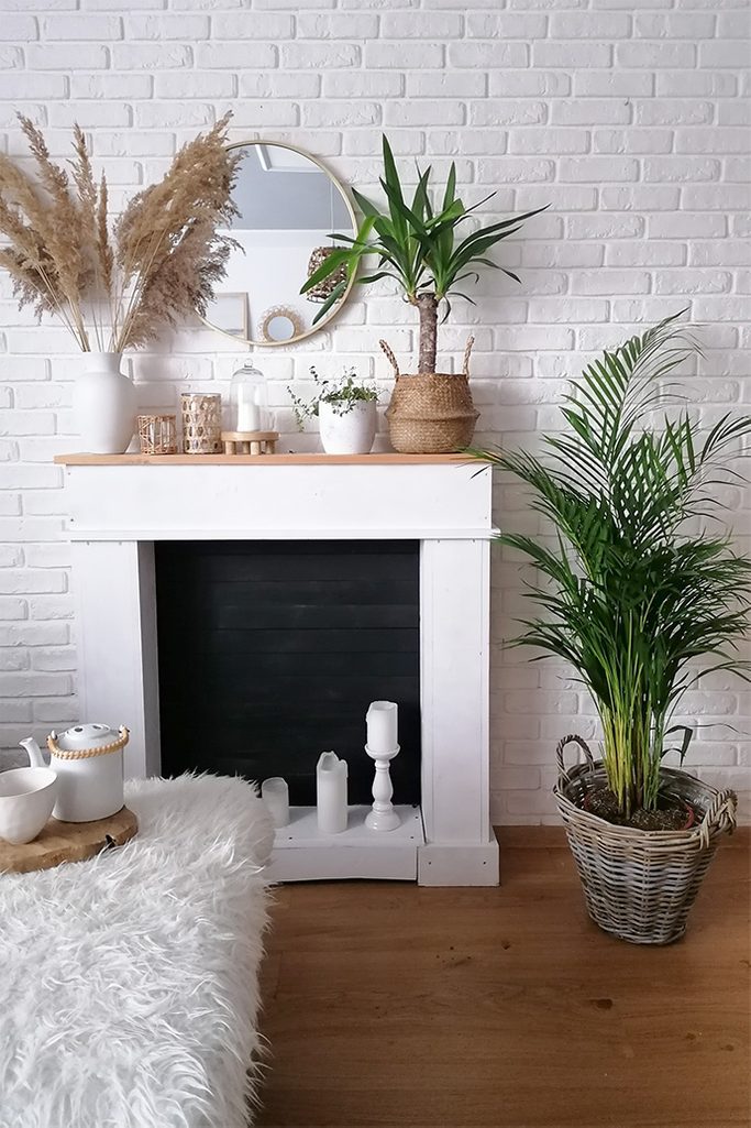 white brick wall, fireplace on a white wall, fireplace decorations, boho style decorations, large decorative plant in a wooden basket as room decoration